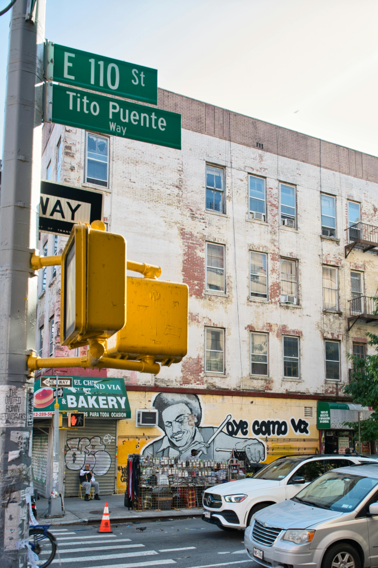 Street view of Tito Puente Way at E 110 St in East Harlem, featuring a vibrant mural.